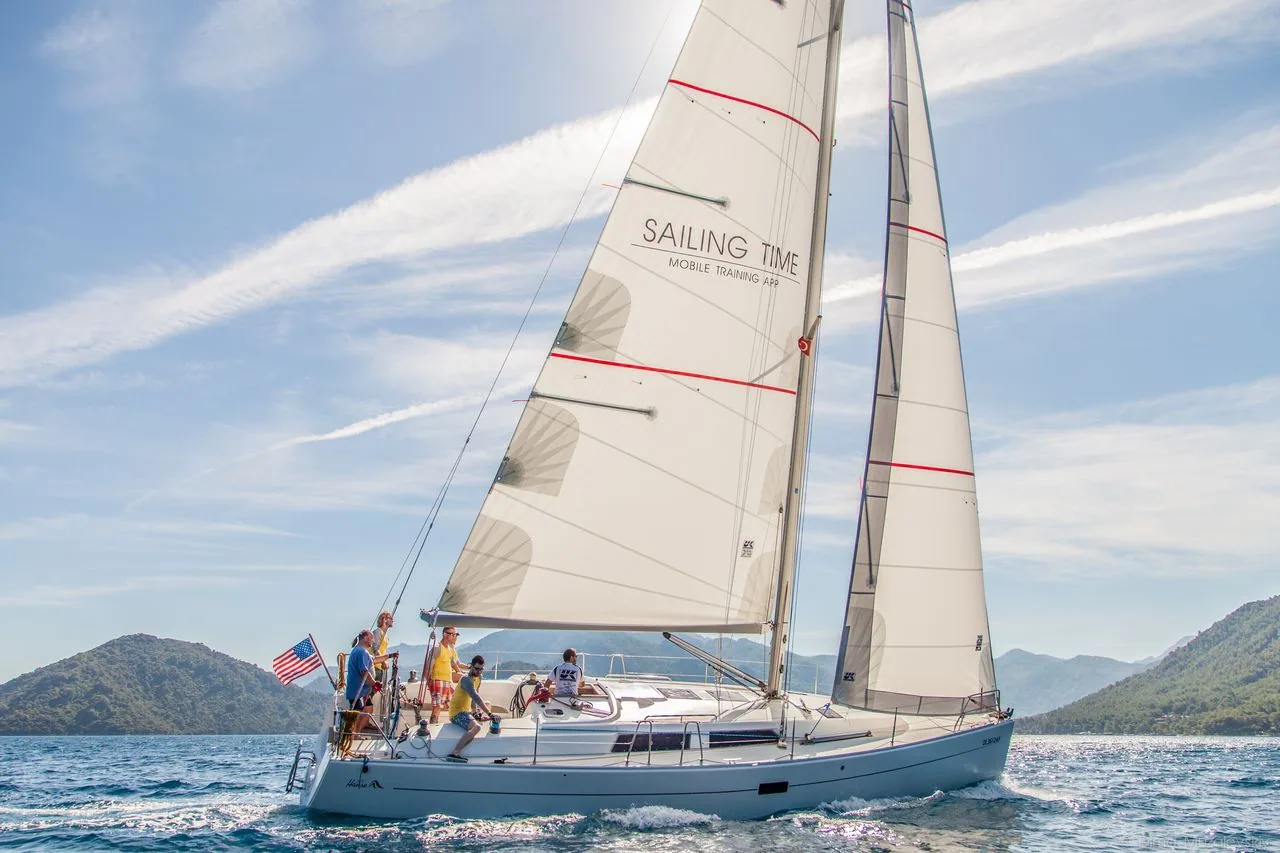 Charter sloop under white Dacron mainsail and jib with family aboard, mountains behind