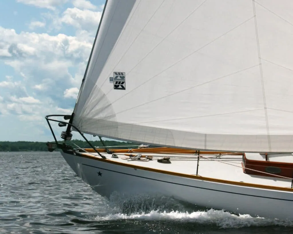 Bow of a classic wooden yacht sailing upwind under a tri-radial Dacron jib with a small logo