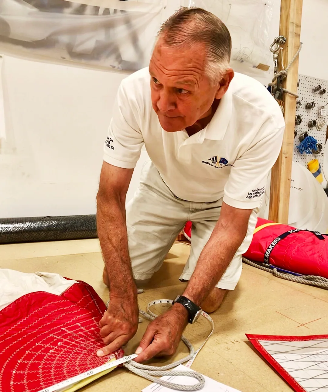 UK Sailmakers loft worker in a company polo inspecting a red sail's reinforcement patch