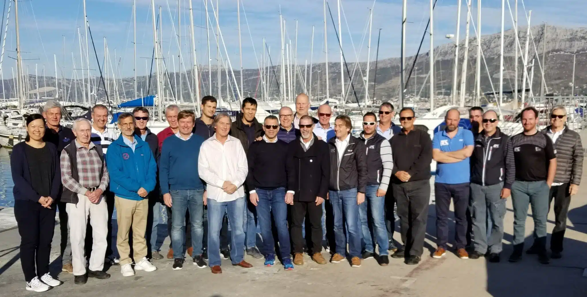 UK Sailmakers managers posed for a group photo at a marina with sailboat masts behind