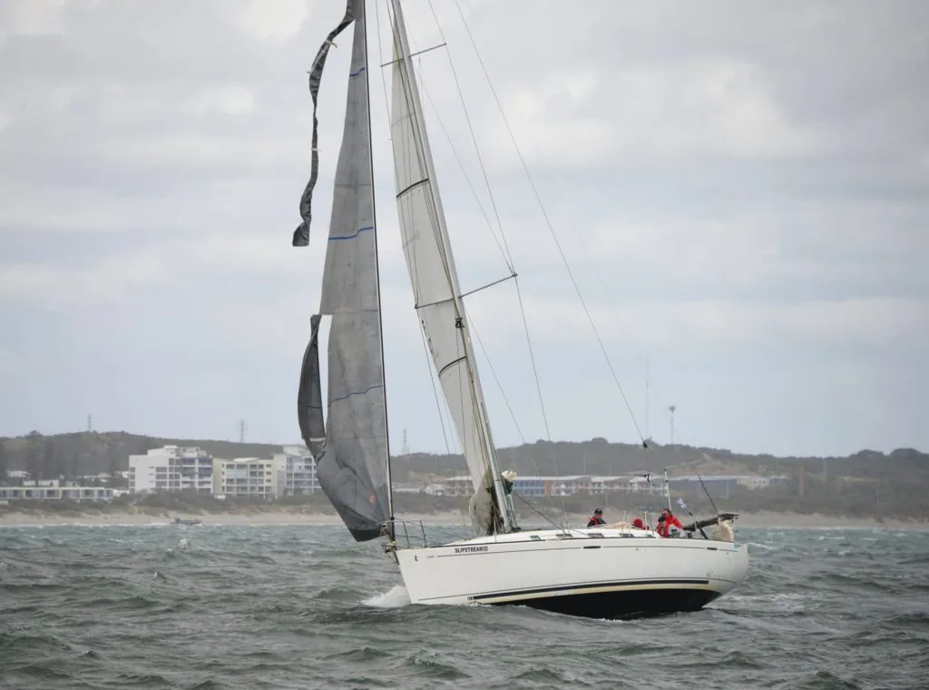 Sailboat crew in red jackets sailing upwind with a torn genoa flapping loose in rough seas