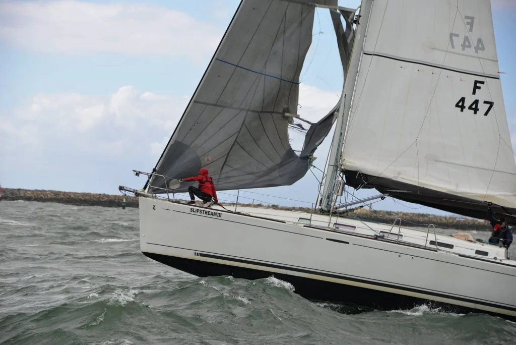 Crew member in red climbing forward to deal with a torn, collapsed genoa near the bow
