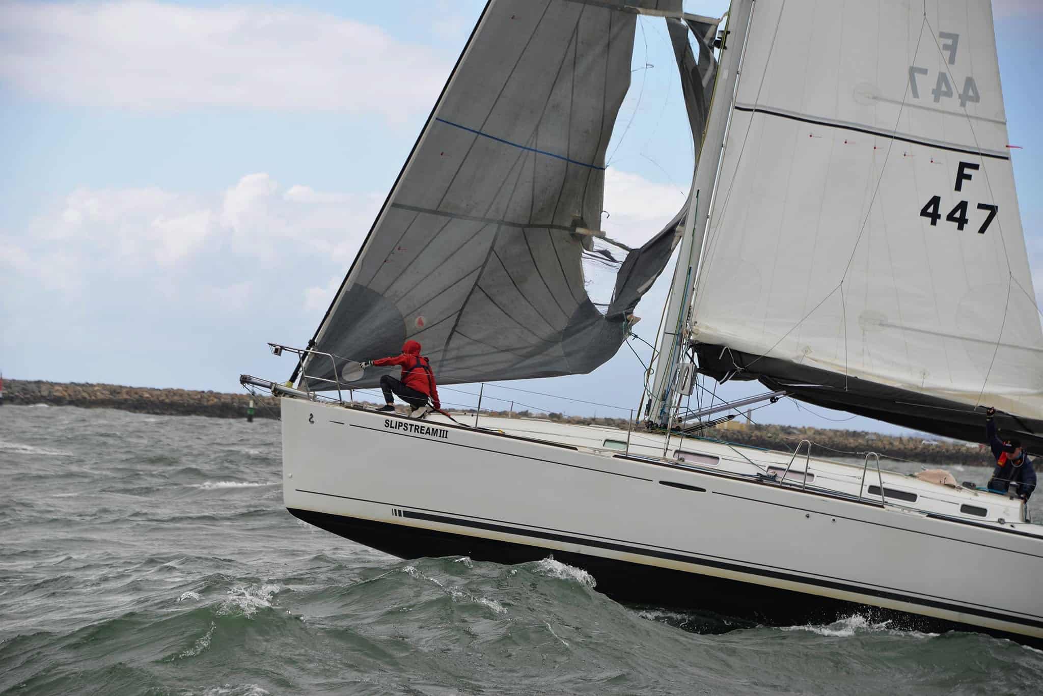 Crew member in red climbing forward to deal with a torn, collapsed genoa near the bow
