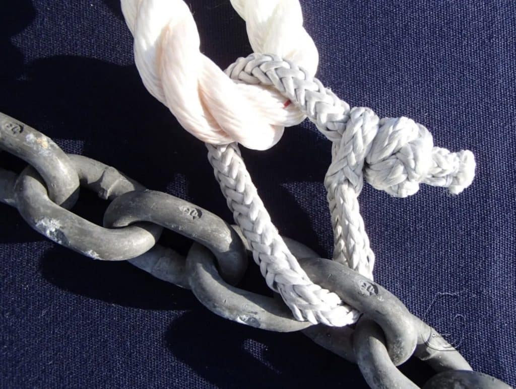 Close-up of an anchor chain tied to a rope snubber with a rolling hitch, lit by low sun