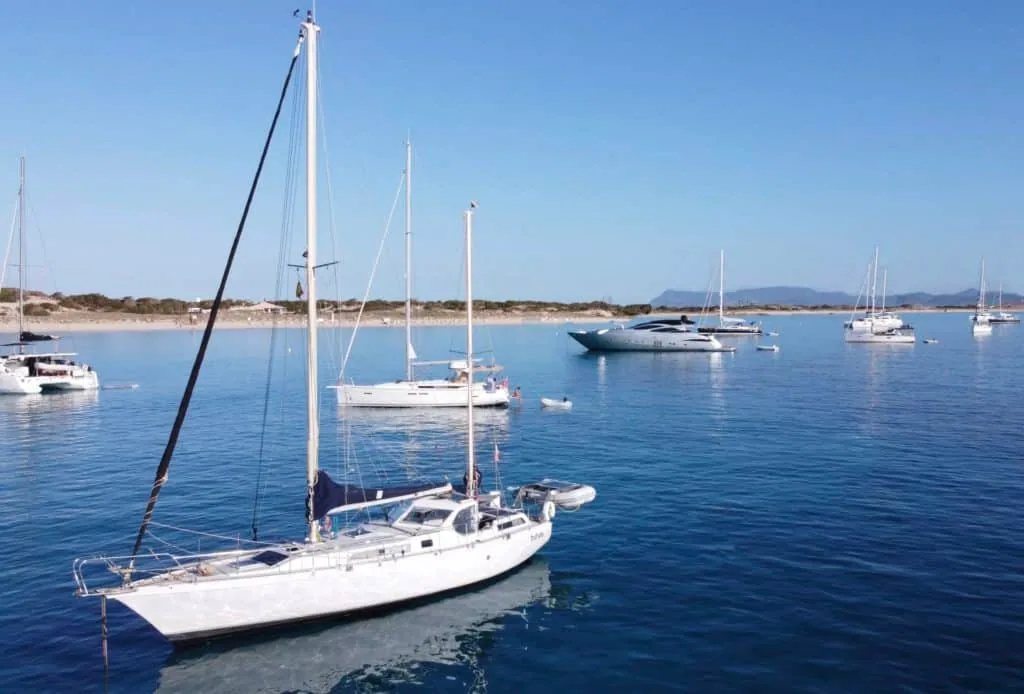 Sailboats and a superyacht anchored in a turquoise bay near a sandy shore