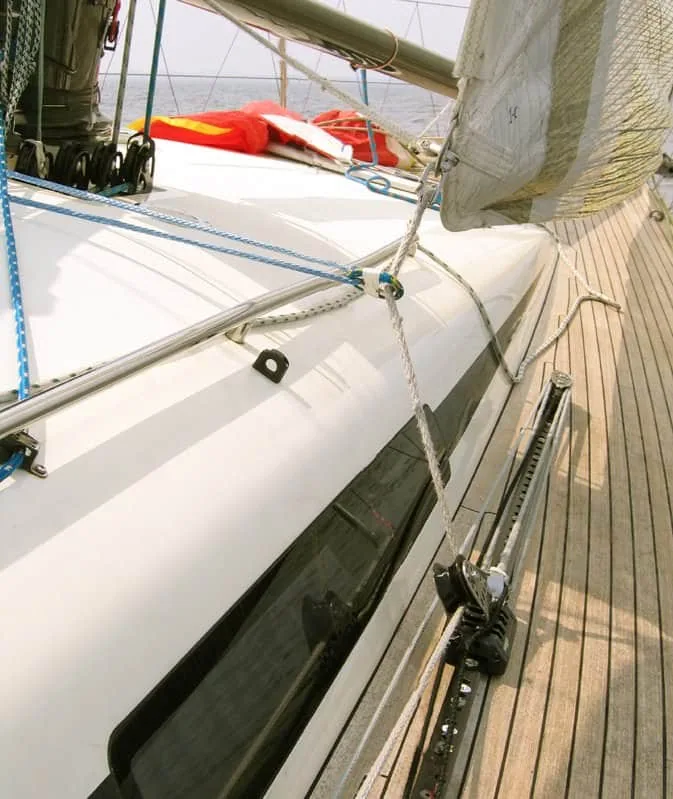 Close-up of a sailboat's teak foredeck showing genoa inhauler track and block hardware