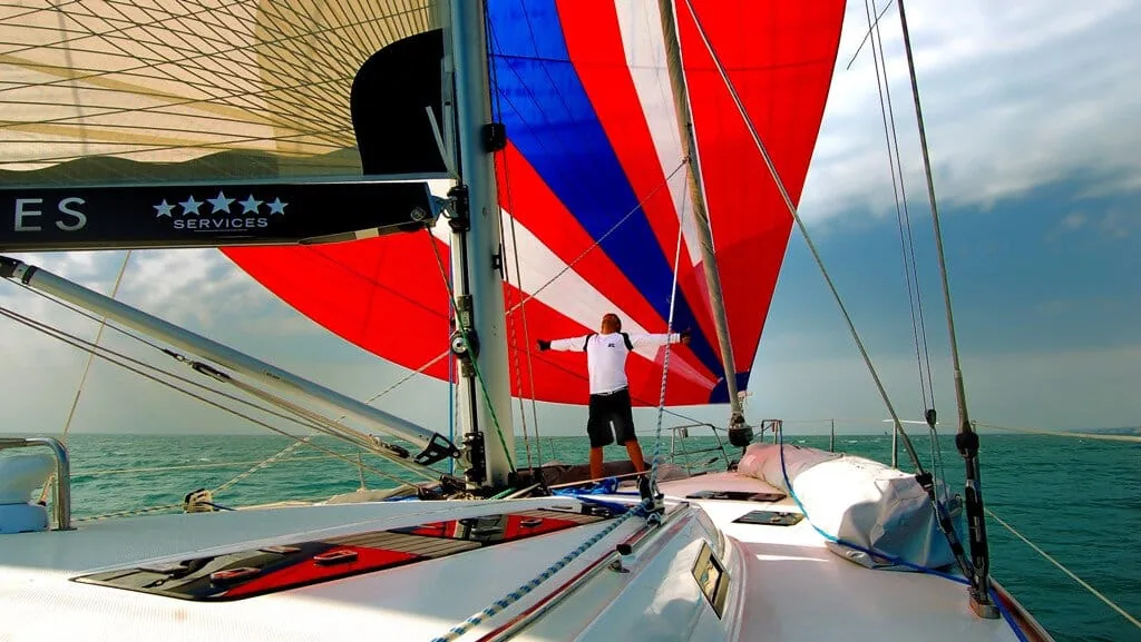 Crew member at the bow of a Beneteau 57 flying a red, white and blue cruising gennaker