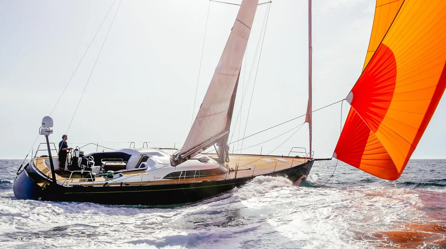 Classic dark-hulled cruising yacht reaching with an orange and red spinnaker filling
