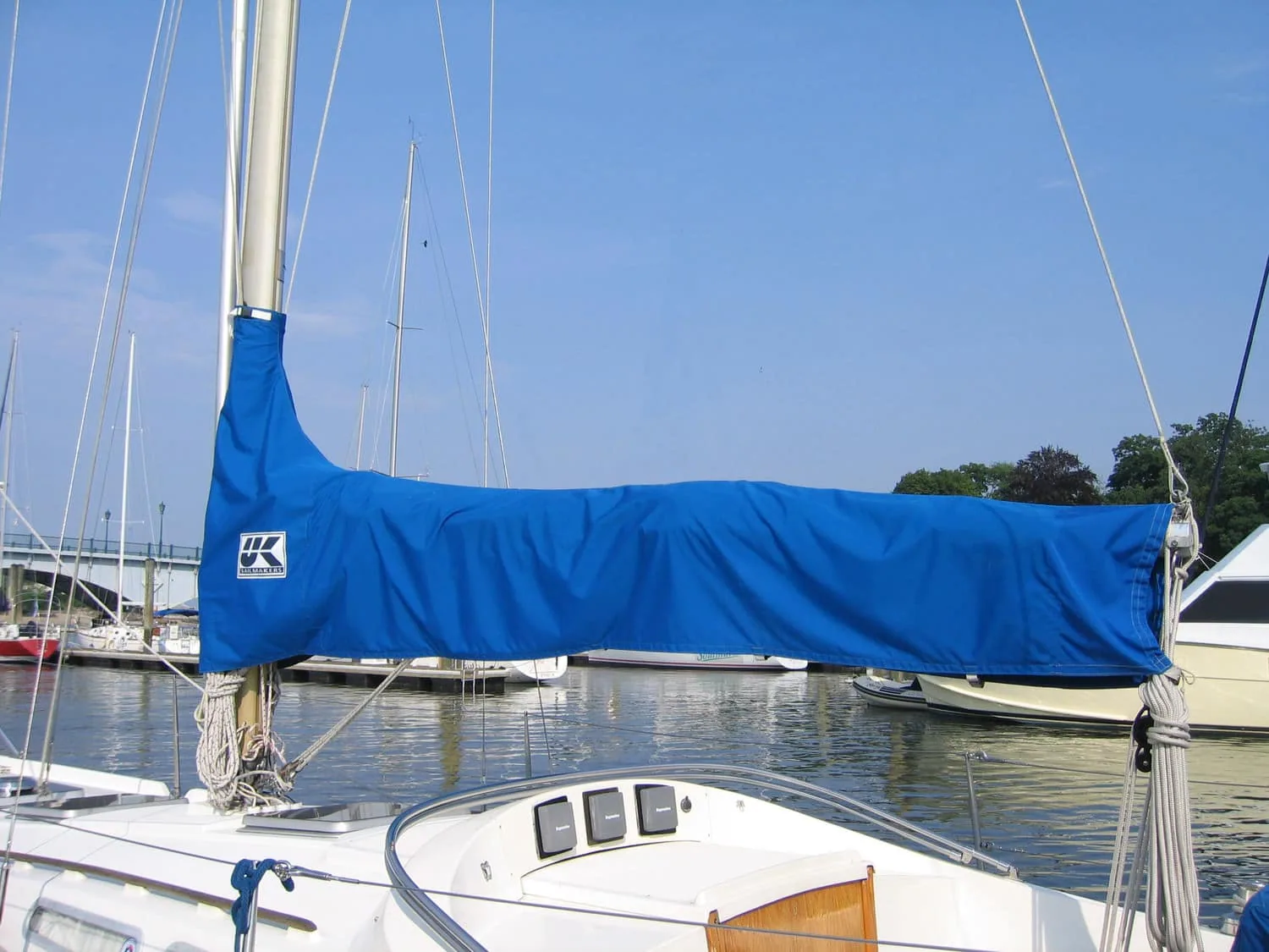 Blue UK Sailmakers sail cover fitted along a boom at a marina dock