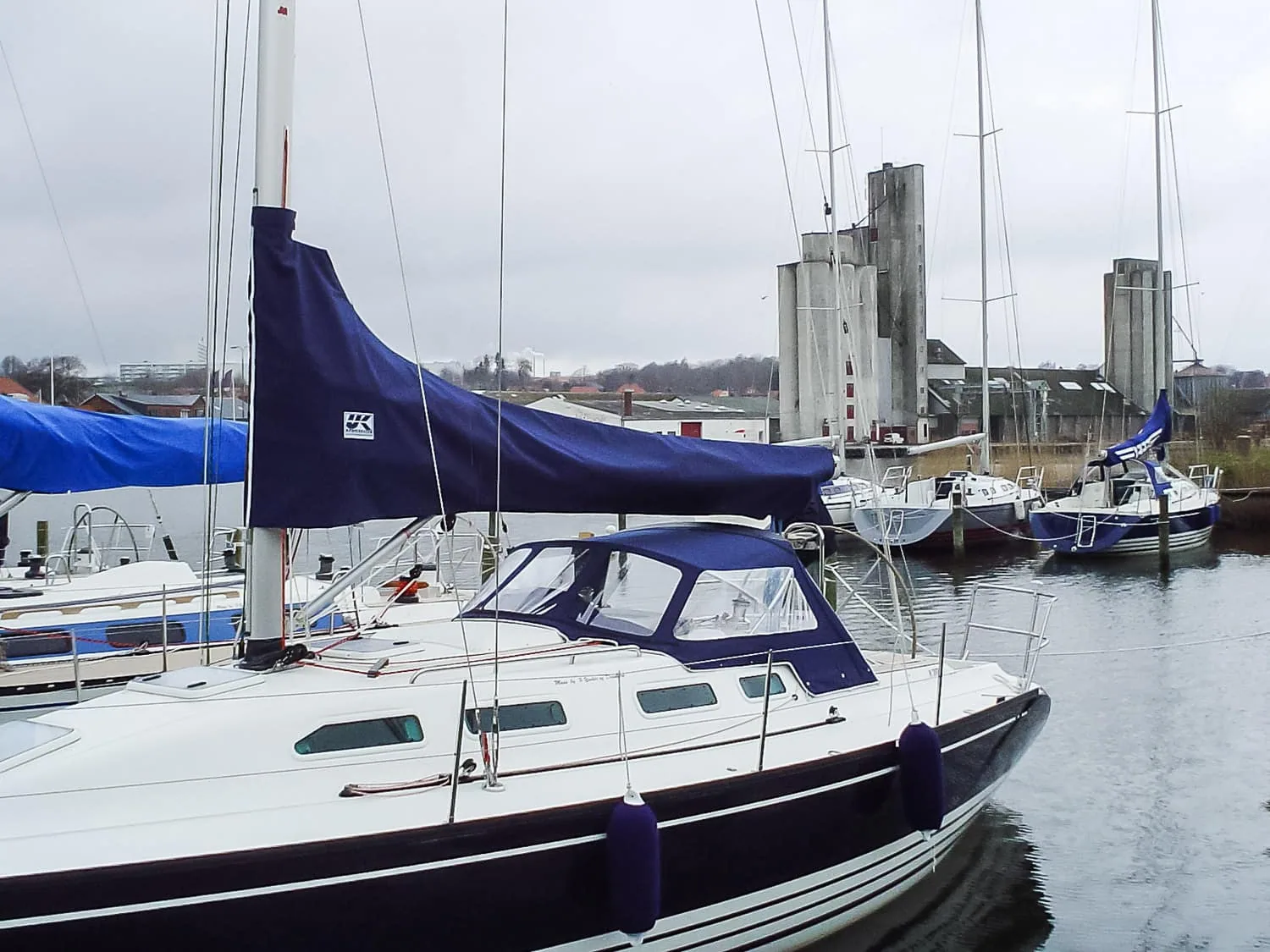 Navy sail cover on the boom of an X-Yacht moored at a marina under grey skies