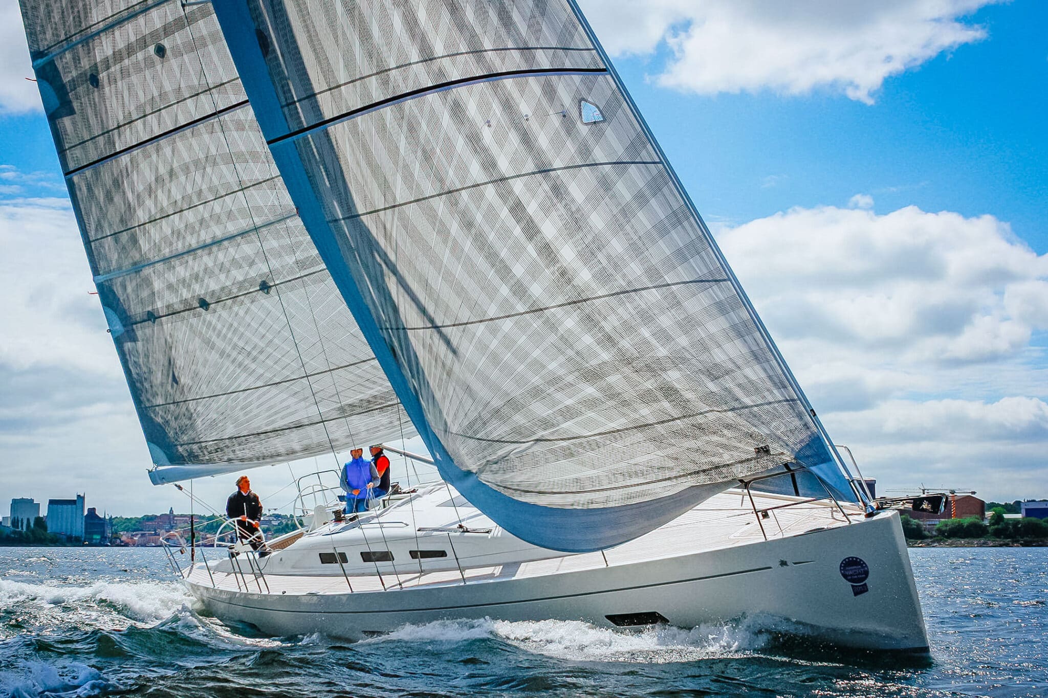 Cruising yacht heeled under an X-Drive® carbon mainsail and genoa, city skyline behind