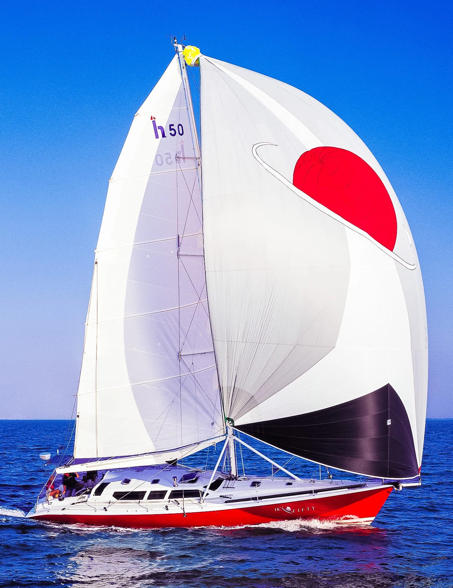 Red-hulled 'Inquisity' (h50) sailing under a white spinnaker with a red circle