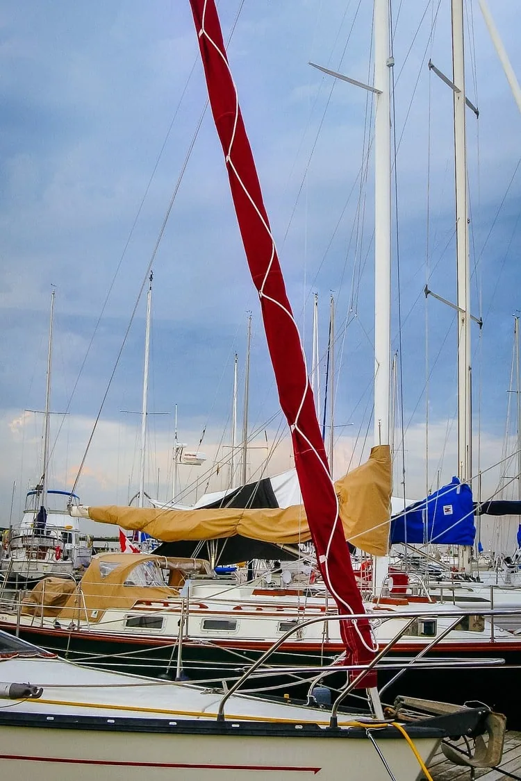 Red jib sock zipped around a furled genoa among masts at a marina