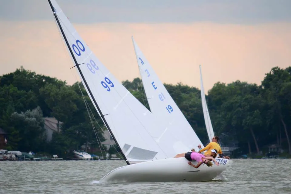 Two C-Scows racing upwind in evening light, sail numbers 99 and 00 visible