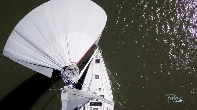 Aerial view of a cruising spinnaker being gathered down into its dousing sock