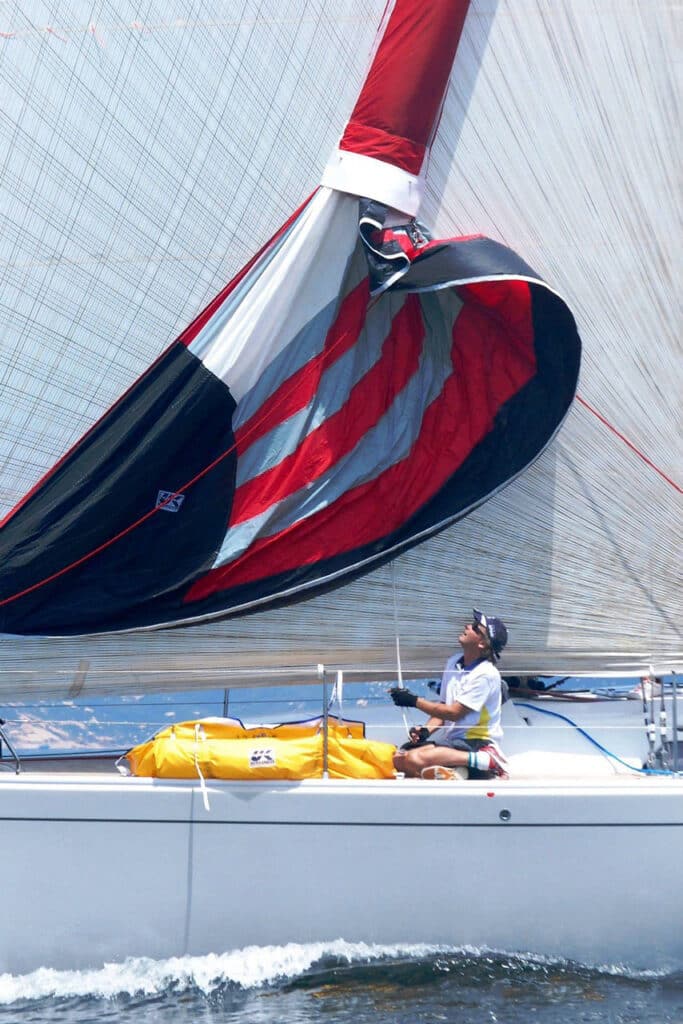 Crew hauling down a red, black and grey striped cruising spinnaker toward its sock