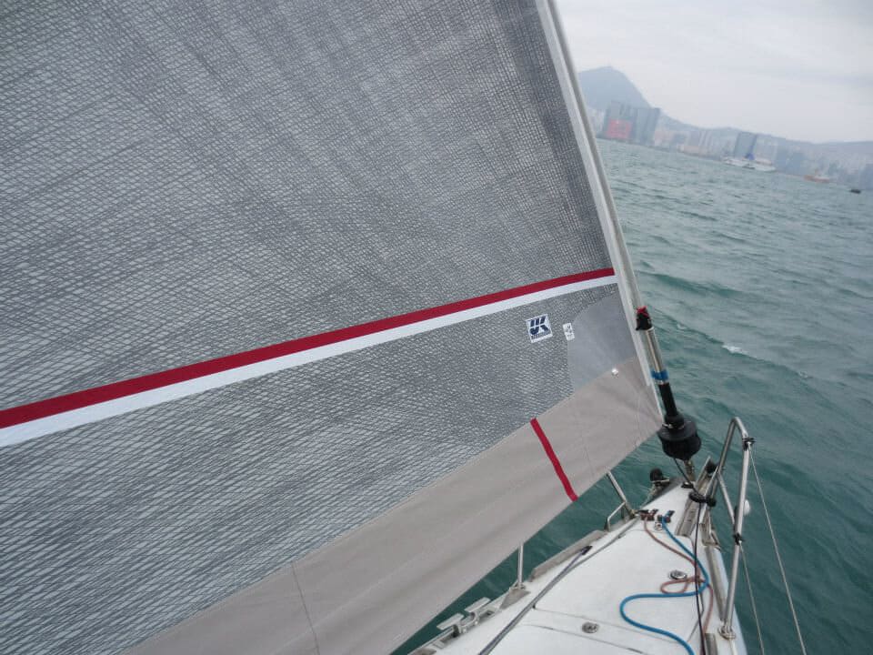 Close-up of a grey Titanium genoa with a red pinstripe UV cover, hazy hills beyond