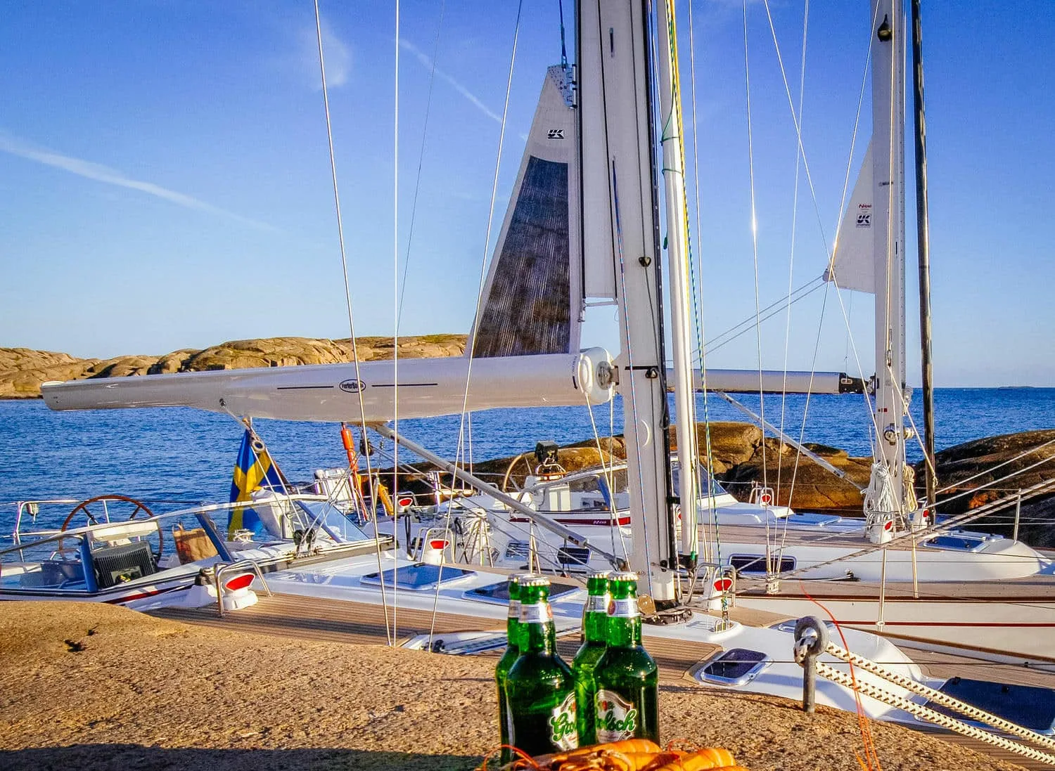 Two small keelboats with furling booms pulled up on a rocky beach, beers in foreground
