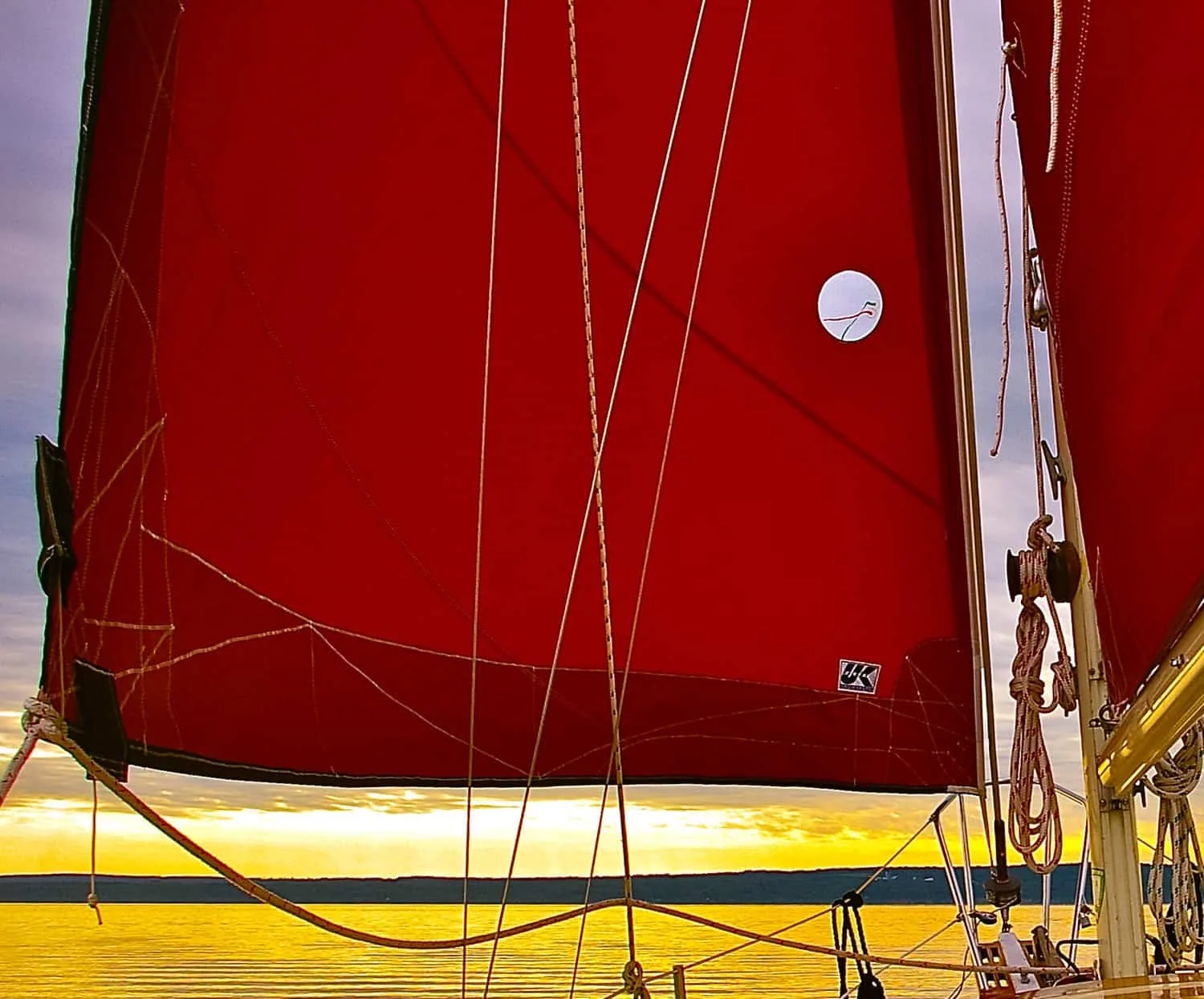 Red sails glowing at sunset with a reflective UK Sailmakers tag on the cloth