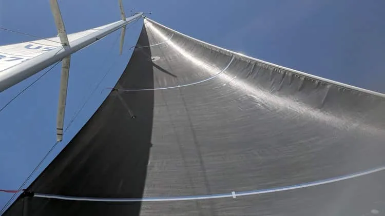 Looking up a J/105 mainsail backlit by the sun against a hazy sky