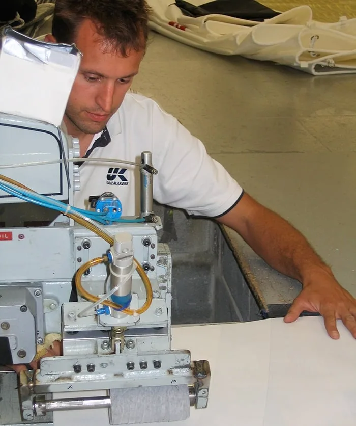 UK Sailmakers loft worker in a company polo operating a sailmaking machine on the floor
