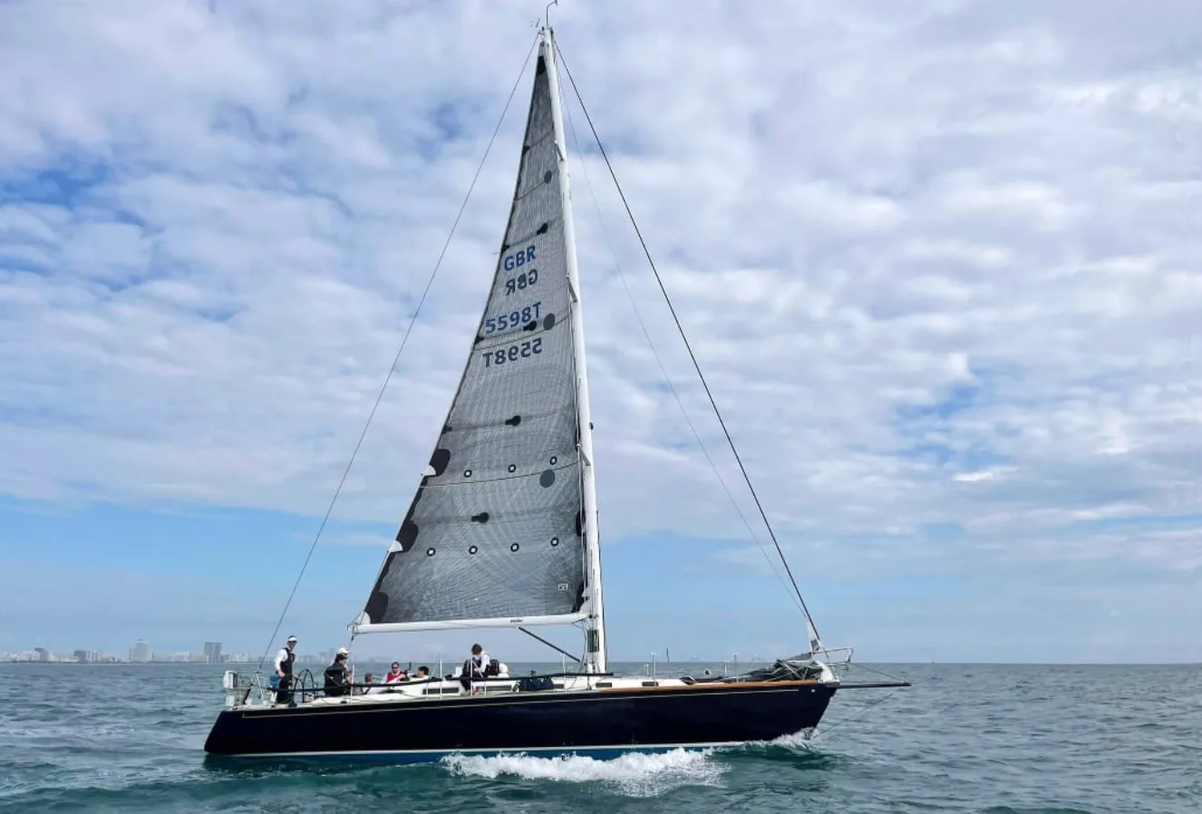 J/44 sailboat GBR 880 heeled over under a grey mesh-look mainsail, crew on the rail