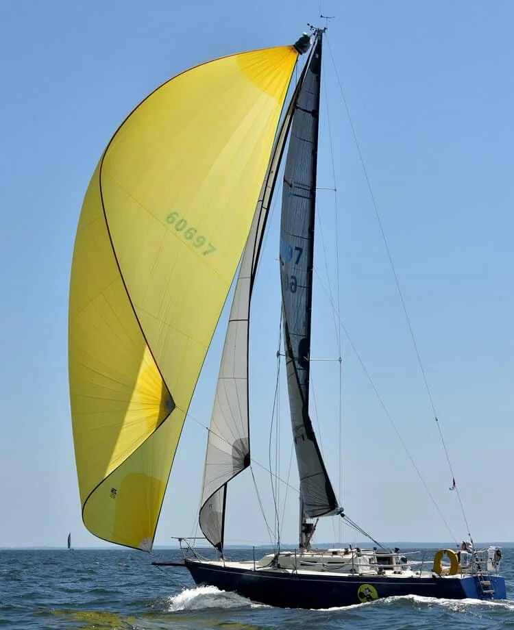 A J/35 flying a yellow spinnaker and Dazy staysail from her fixed bowsprit