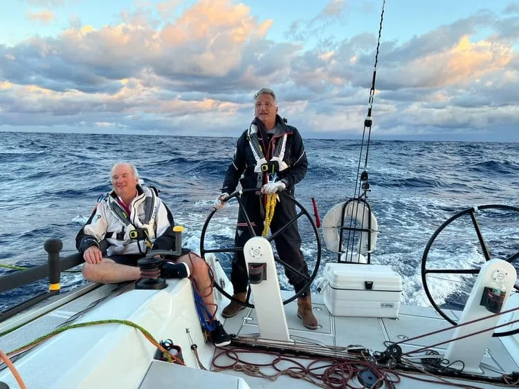 Two sailors at the wheels of an offshore racing yacht at dusk, in foul-weather gear