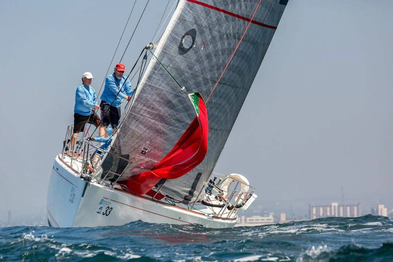 Racing sailboat with a red spinnaker peeking from the bow, city skyline in the distance
