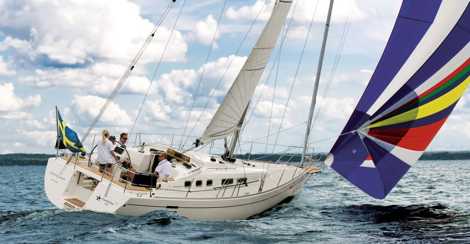 Cruising sailboat under sail with a colorful spinnaker set to starboard, Swedish flag flying