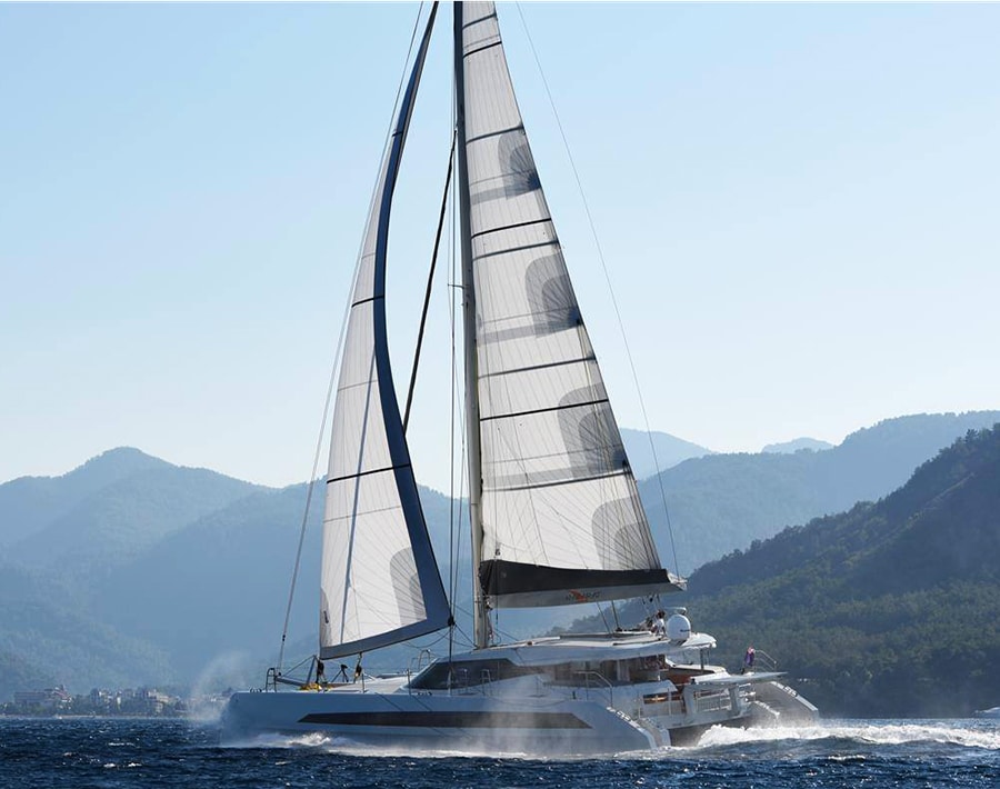 Cruising catamaran under sail near a mountainous coastline in Türkiye