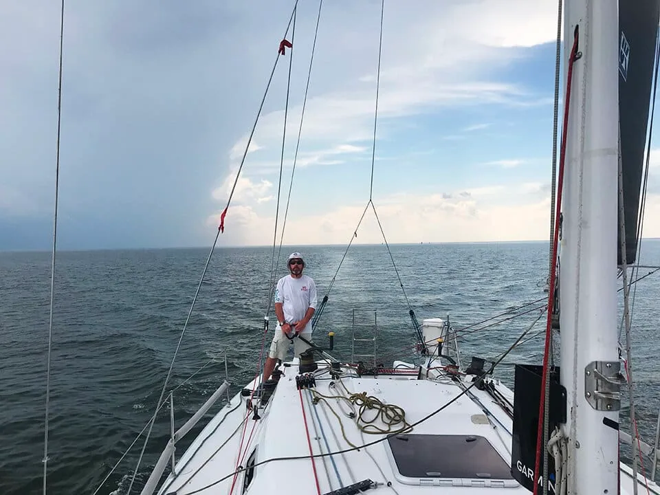 Sailor at the helm on a doublehanded race with a dark squall building astern