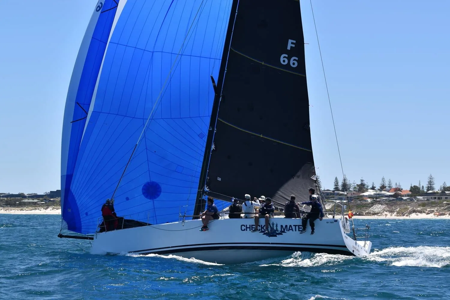 King 40 Checkmate racing under blue spinnaker and dark mainsail near the coast