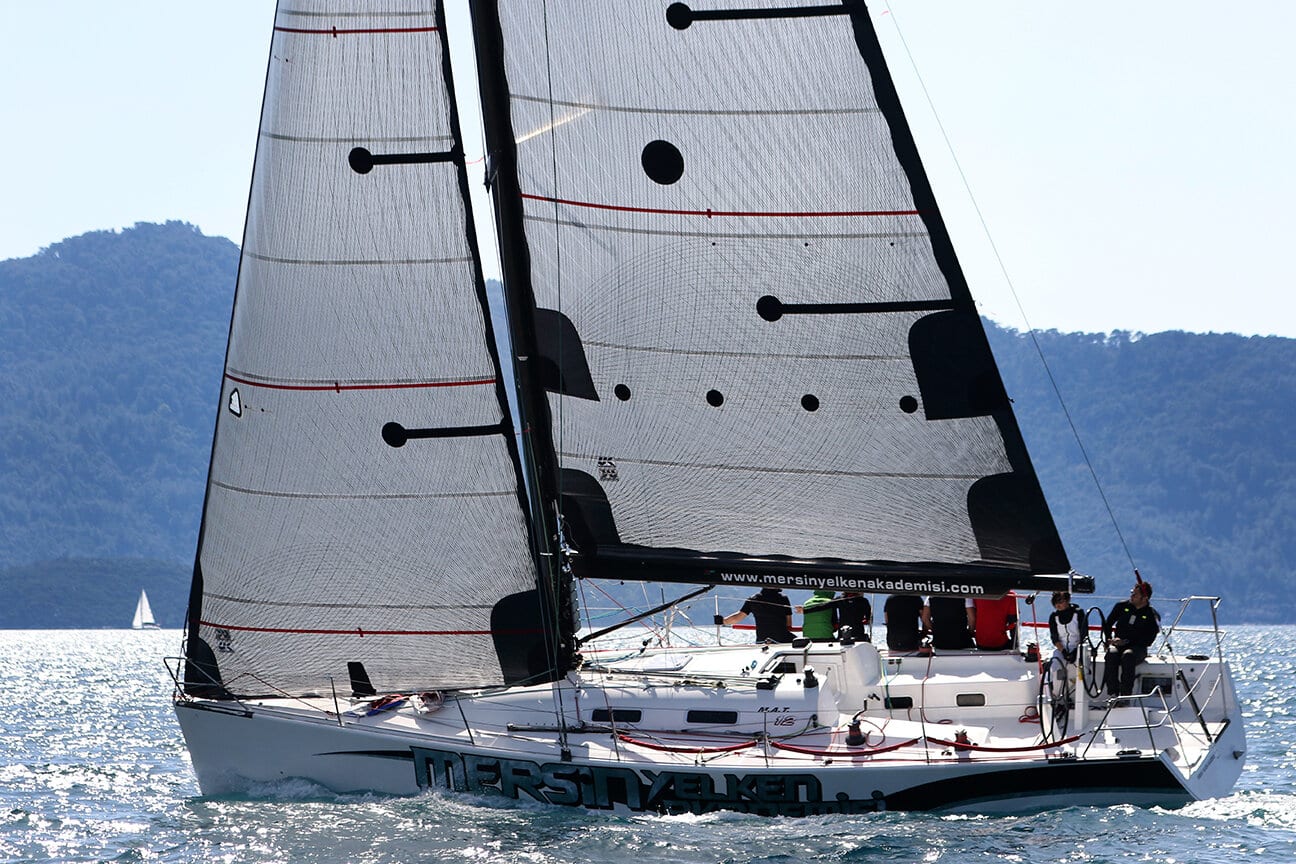 Racing sport boat under black sails off the Turkish coast, hillside town behind