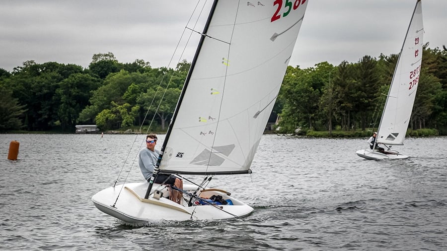 Scow-hulled sailboats racing on an inland lake, sail number 2565 leading