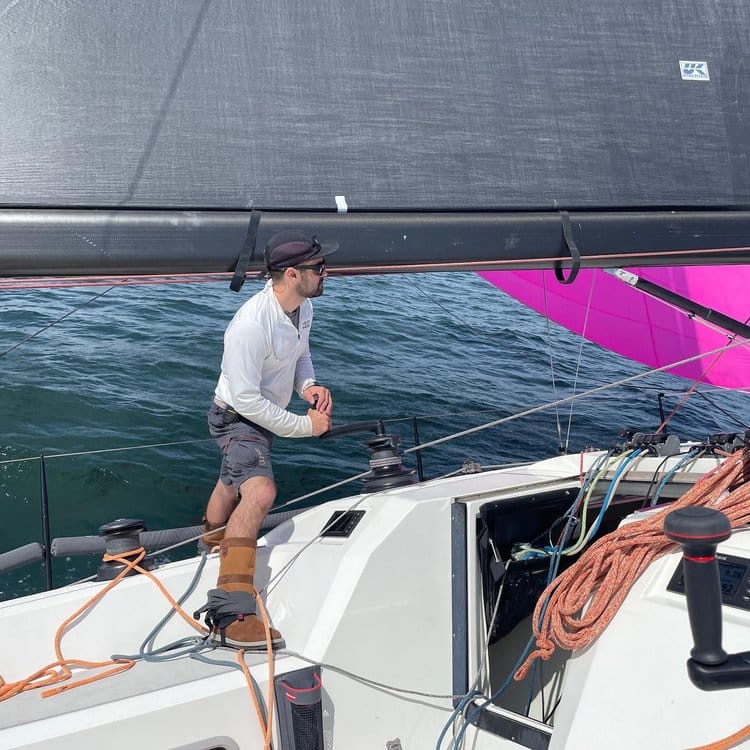 Morgan Bennett grinding a winch on the rail as a pink spinnaker flies behind him