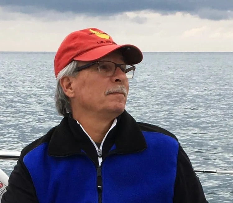 Portrait of a man in a red cap and blue jacket aboard a boat on open water