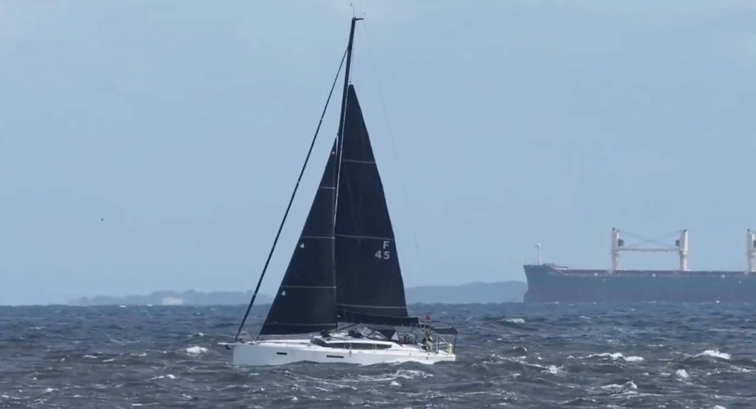 JPK 45 Sirene sailing under a dark mainsail with a cargo ship on the horizon