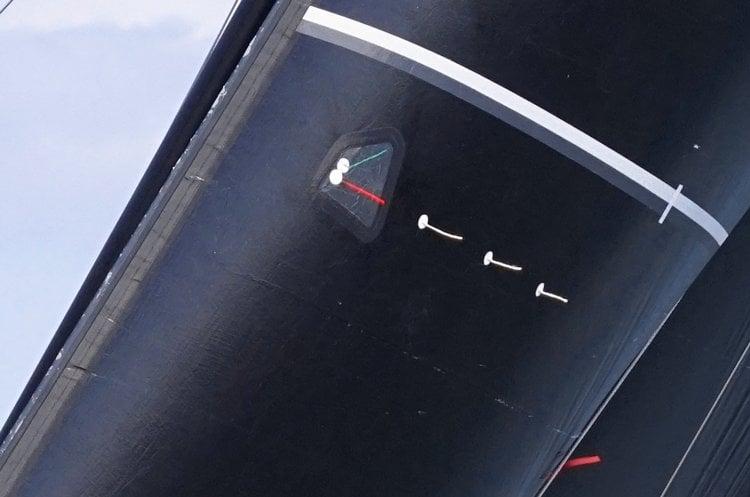 Close-up of leech telltales and a small wind-direction instrument on a dark sail