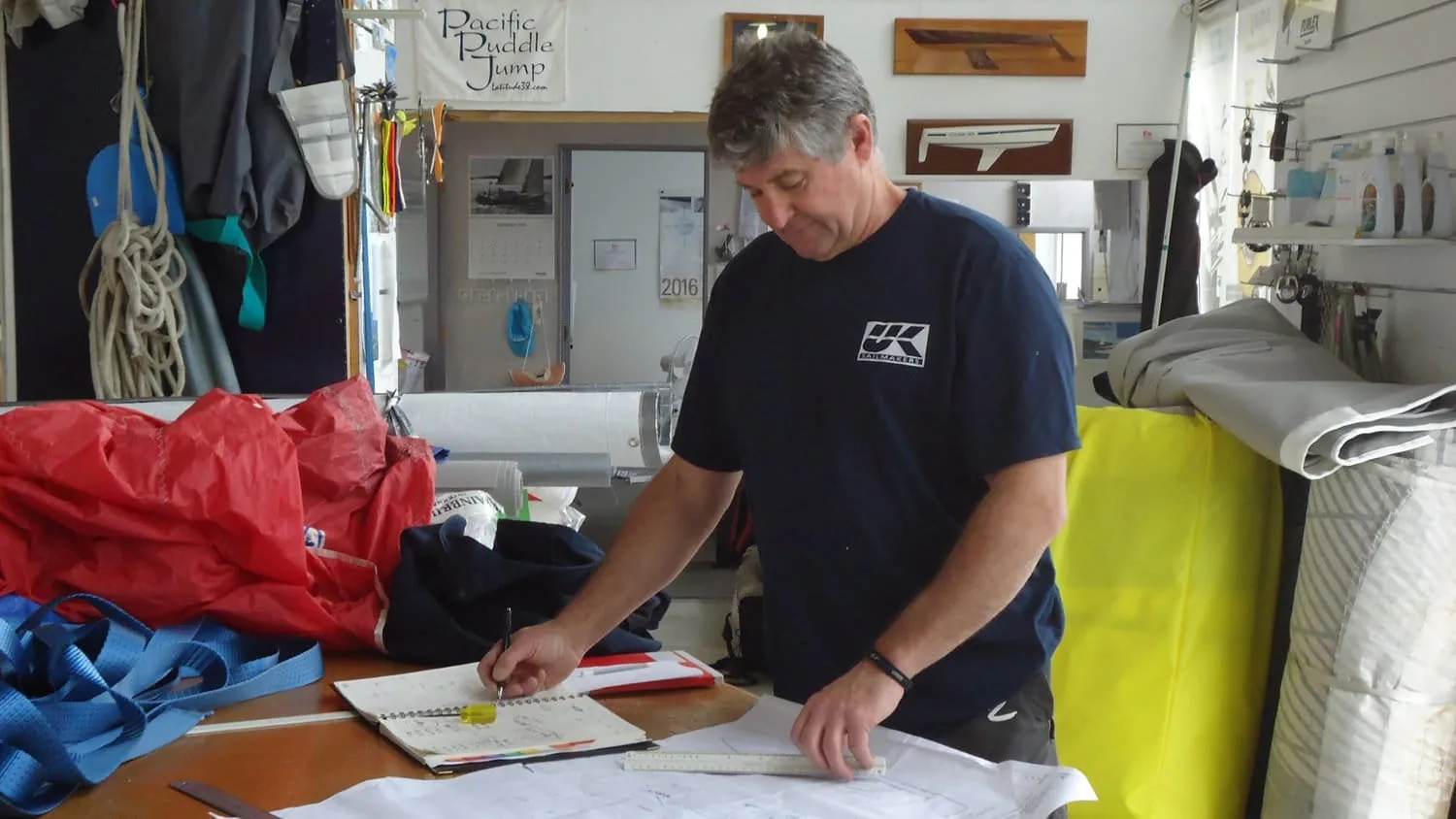 Sailmaker marking up a sail plan at a loft workbench in a UK Sailmakers polo shirt