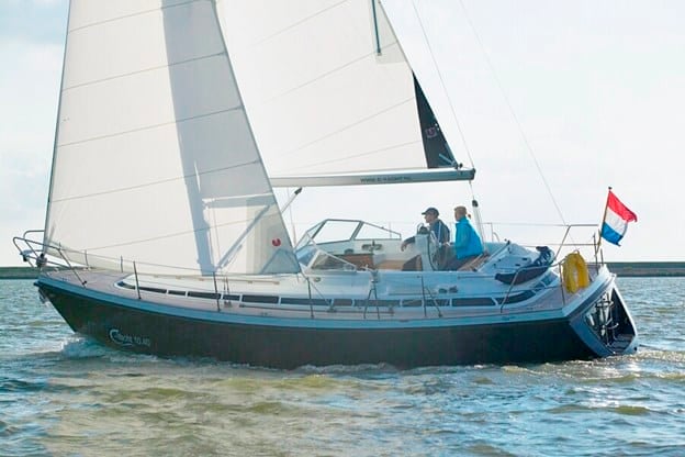 Cruising sailboat flying a Dutch flag under full sail with two crew relaxing aboard