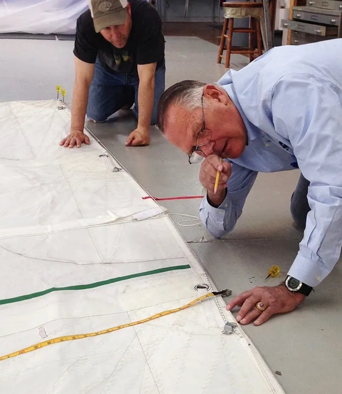 Two sailmakers marking up a mainsail on the loft floor with pencil and measuring tape