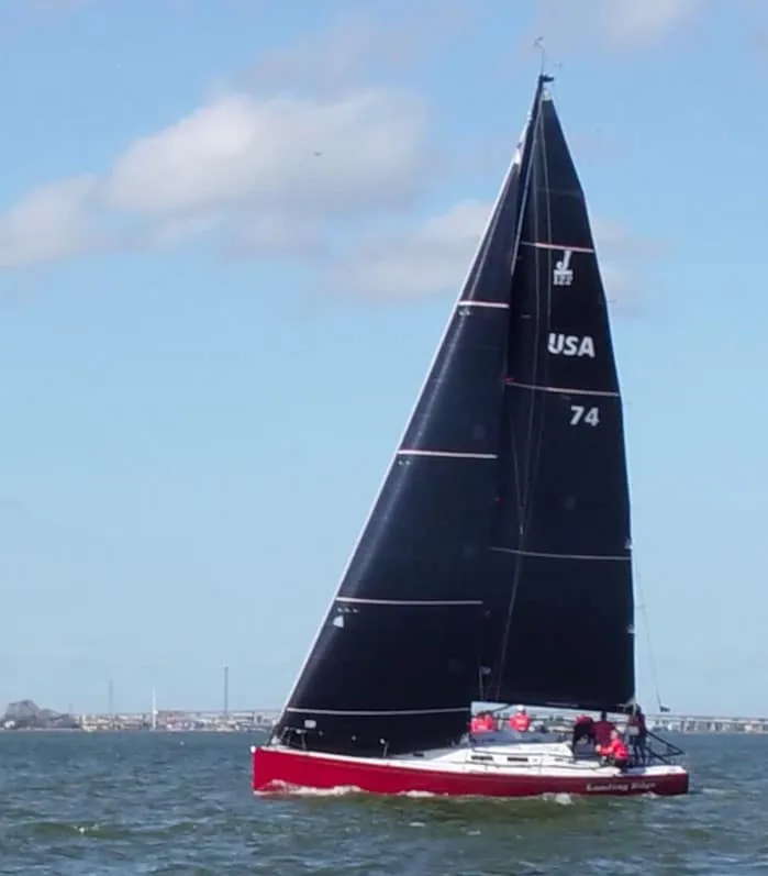 Red-hulled sportboat, sail number USA 74, racing under a black mainsail at J/Fest