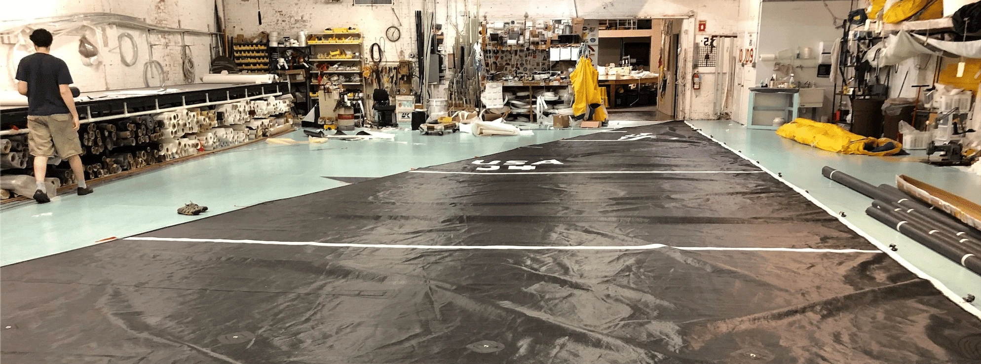 Large dark sail laid out across a sail loft floor for finishing work