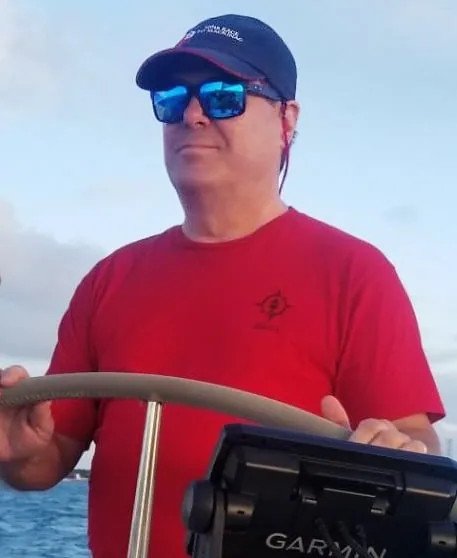 Tom Spees at the helm wearing sunglasses and a red shirt, Garmin display in view