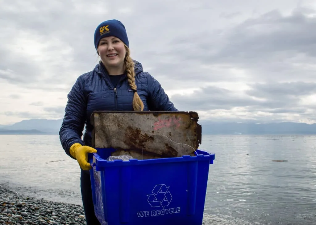 Volunteer holding a recycling bin of debris collected on a rocky beach cleanup