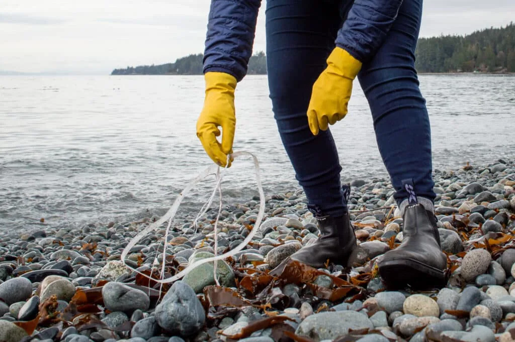 Volunteer in yellow gloves picking up rope debris on a rocky shoreline