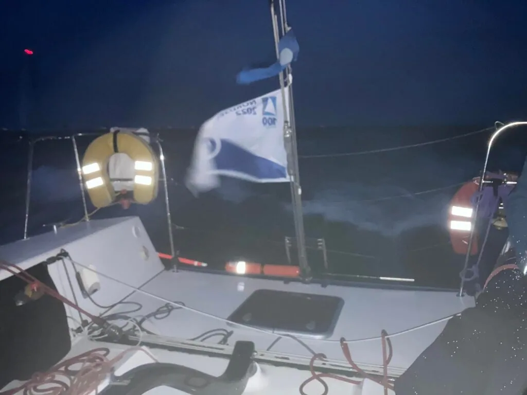 Boat's stern and wake lit by deck lights during a night race