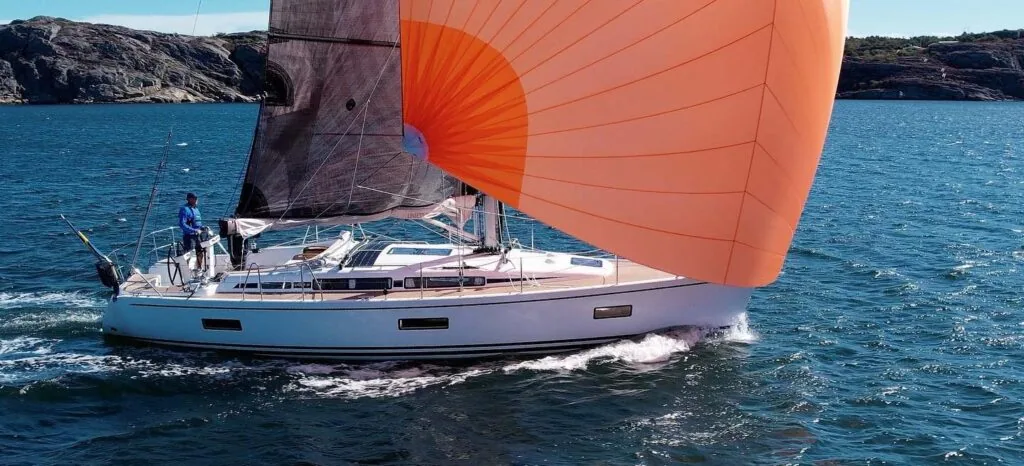 Cruising sailboat flying an orange asymmetric spinnaker along a rocky coast