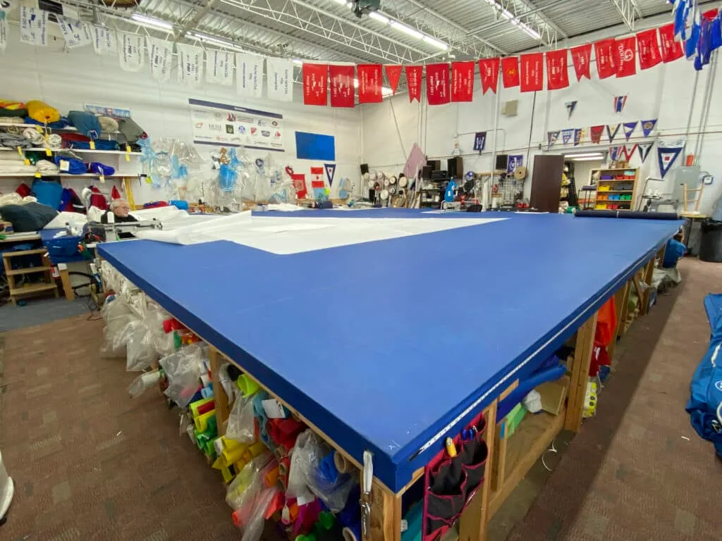 Sailcrafters loft floor with a blue sail laid out beneath racing pennants
